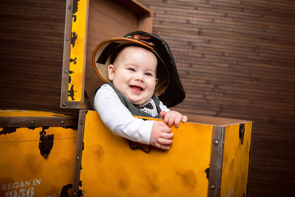 Ein Baby mit einer viel zu großen ledernen Schirmmütze sitzt in einer gelben Box.
