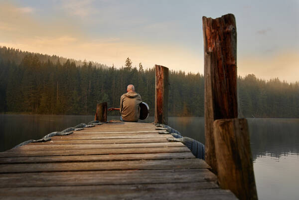 Der steirische Musiker Martin Moro sitzt im Abendlicht mit einer Gitarre auf einem hölzernen Anlegesteg an einem See.