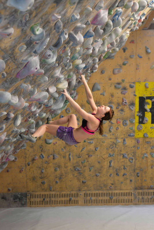 Eine junge Frau klettert in einer Kletterhalle an einem Überhang.