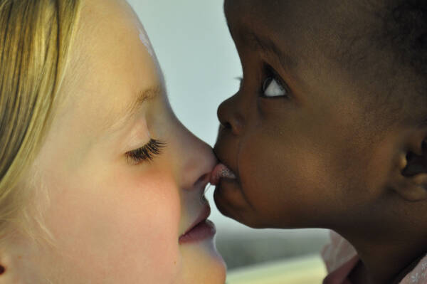 Ein dunkelhäutiges Kind schleckt einem hellhäutigen Kind über die Nase.