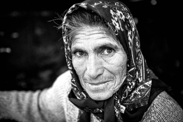 Nahaufnahme einer alten Frau mit geblümtem Kopftuch und Strickweste. Schwarz-Weiß.