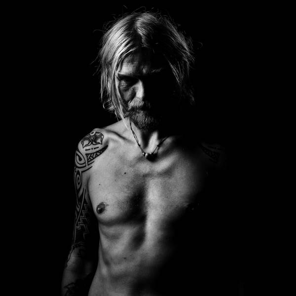 Low-Key-Portrait eines bärtigen Mannes mit nacktem Oberkörper und  tribal Tatoos auf Schulter und Arm.