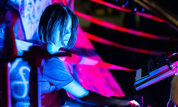 Die Musikerin Yulan Yu bei einem Auftritt, mit blauem und magentafarbigem Licht angestrahlt.