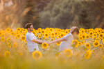 Ein Paar in weißem Gewand steht in einem Sonnenblumenfeld und hält sich an den Händen.