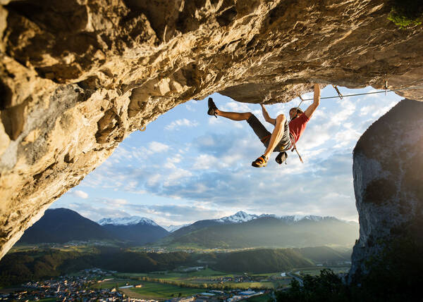 Kletterer an einem Überhang in der Grottenwand mit Blick auf die Hauptwand der Martinswand, Selrain und die Stubaier Alpen.