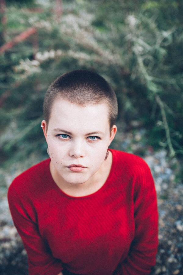 Portrait einer jungen Frau mit sehr kurzen Haaren und rotem Pullover, die direkt in die Kamera schaut.