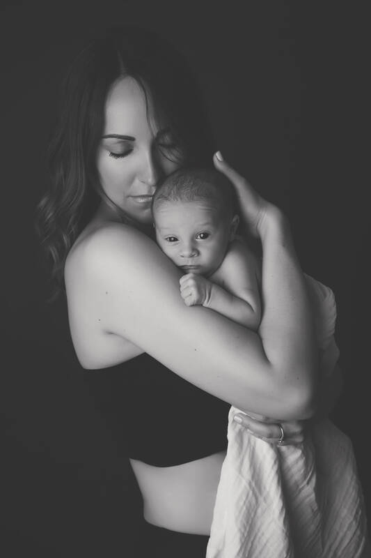 Eine Frau mit einem sehr jungen Baby am Arm. Die Frau hat den Blick gesenkt, das Baby schaut in die Kamera. Schwarz-Weiß.