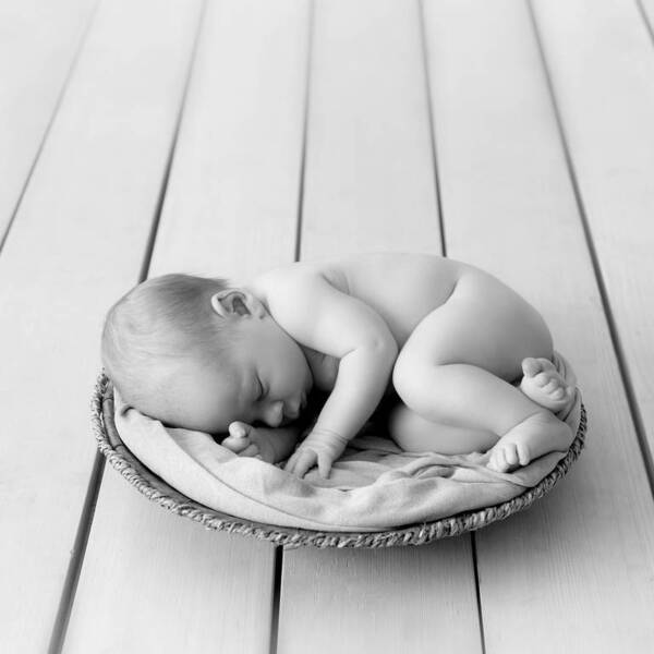 Ein Baby schläft zusammengerollt in einem Korb. Shwarz-Weiß.