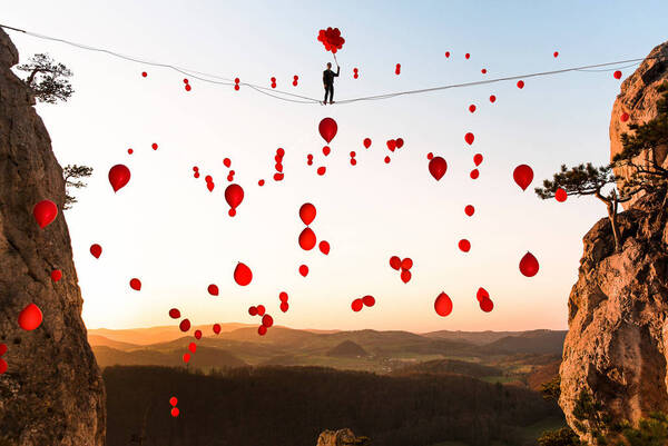 ein Mann auf einem Seil über eine Schlucht mit roten Luftballons.