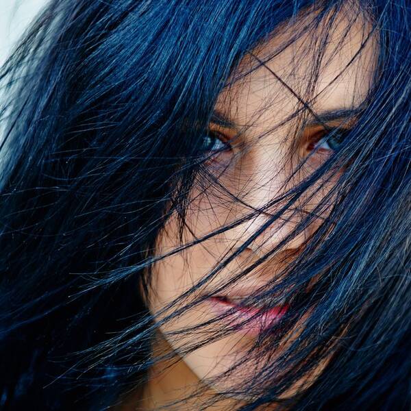 Portrait einer Frau, der Die blauschwarzen Haare über das Gesicht hängen.