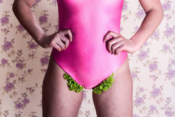 Eine Frau in pinkem Badeanzug. Im Schritt quillt grüner Salat hervor.