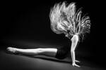 Ein Mädchen in Trikot und Ballerinas macht eine Bodenübung und wirft die langen blonden Haare in die Luft. Schwarz-Weiß.