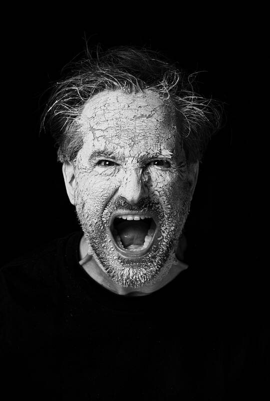 Portrait eines schreienden Mannes, dessen dicke, weiße Schminke bereits abbröckelt. Schwarz-Weiß.