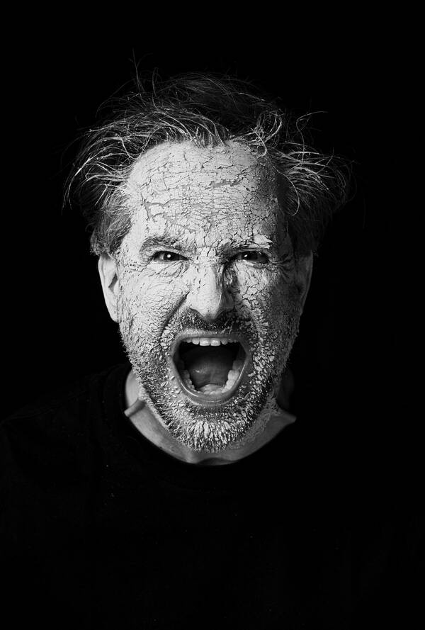 Portrait eines schreienden Mannes, dessen dicke, weiße Schminke bereits abbröckelt. Schwarz-Weiß.