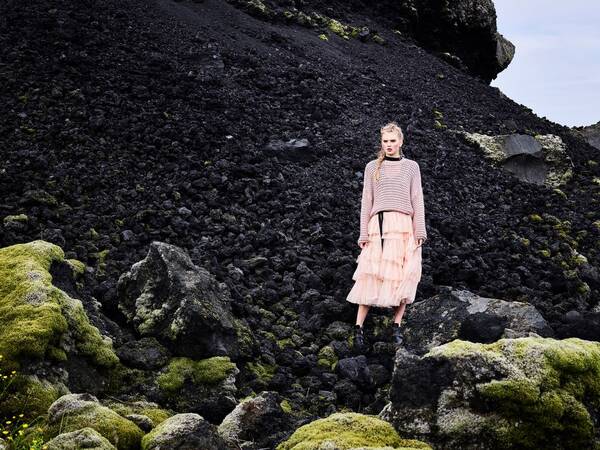 Ein Model in Lachsfarbigem Outfit auf einem Lavaschüttkegel mit bemoosten Steinen.
