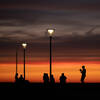 Silhouetten mehrerer Menschen im Abendlicht unter bereits leuchtenden Straßenlaternen.