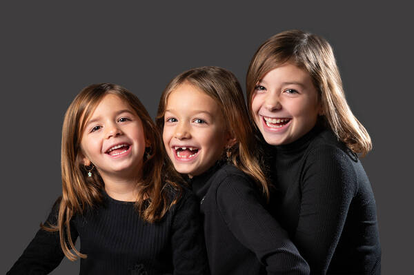 Porträt von drei lachenden Mädchen in schwarzen Pullovern vor dunkelgrauem Hintergrund.