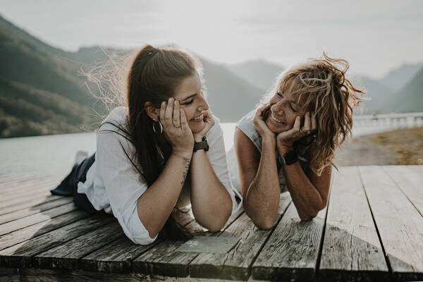 Portrait zweier Frauen, die auf den Planken eines Steges an einem Bergsee liegen.