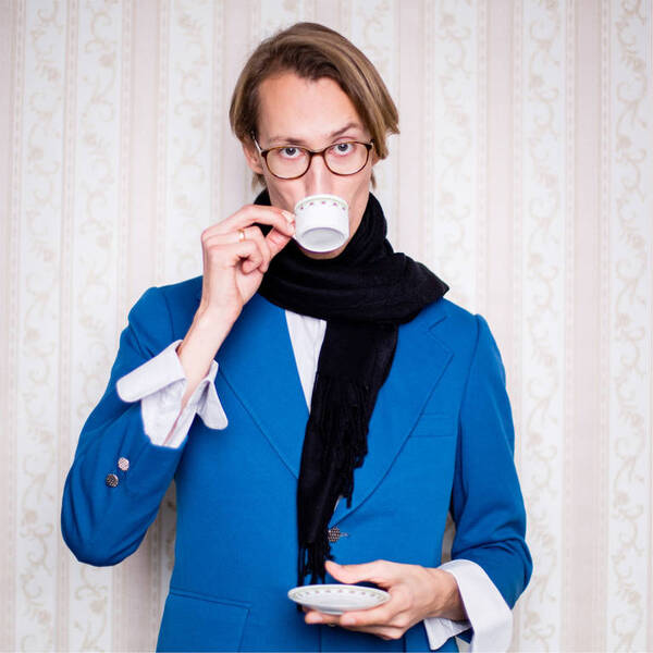Mann in blauem Sakko und schwarzem Schal trinkt aus einer Tasse.