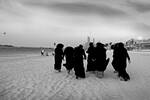 mehrere Nonnen gehen im schwarzen Habit über einen Sandstrand. Schwarz-Weiß