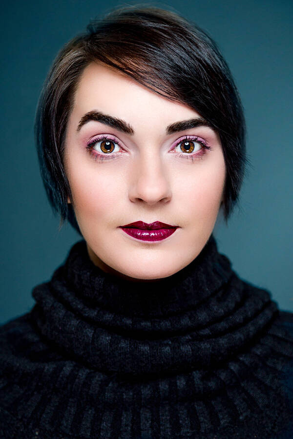 Frontales Portrait einer jungen Frau mit kurzem dunklen Bobtail und dunkelrot geschminkten Lippen.