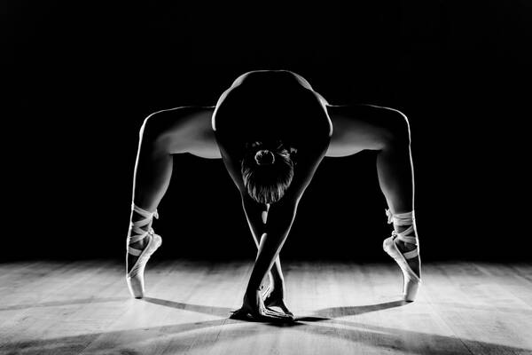 Schwarz-Weißbild einer Ballett-Tänzerin in symmetrischer Position mit spannender Lichtführung