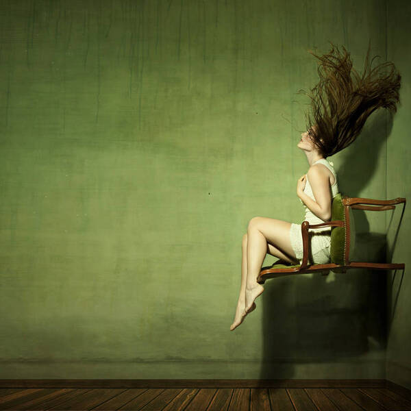 Eine Frau sitzt auf der Lehne eines Sessels der an der Wand steht.