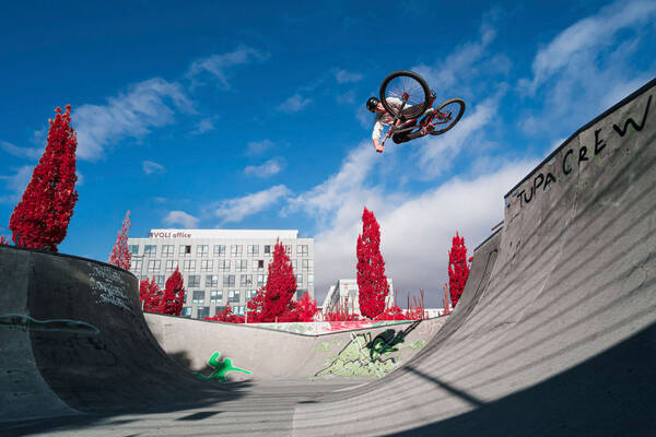 Ein Biker schwebt im Sprung in der Luft über dem Bike-Park beim Tivoli in Innsbruck. Die Bäume und Sträucher sind rot eingefärbt.