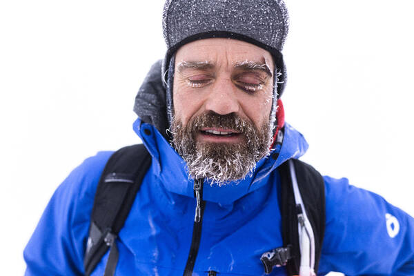 Ein Mann mit winterlicher Bergausrüstung. Bart, Augenbrauen und Wimpern sind mit Eiskristallen bedeckt.