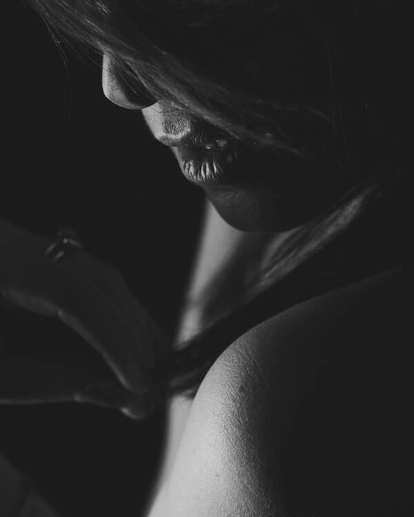 Low-Key Close-Up-Aufnahme einer Frau, die mit ihren Händen nach einer Haarsträhne an ihrer Schulter greift. Schwarz-Weiß.