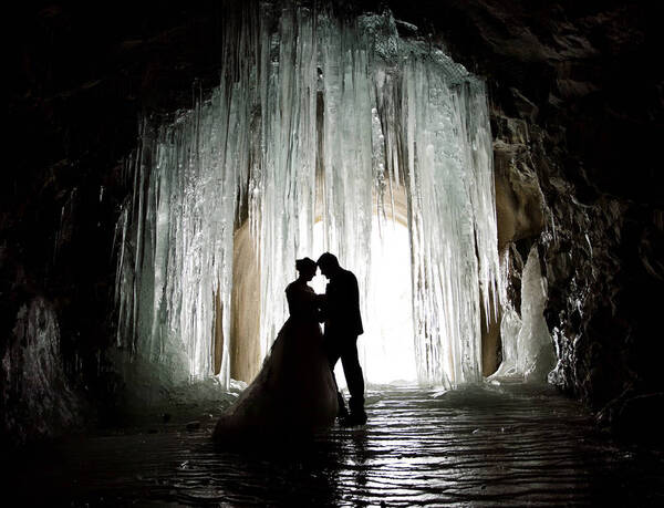 Silhouette eines Hochzeitspaares vor den Eiszapfen einer Eishöhle.