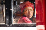 Eine Asiatische Person mit roter Jacke und roter Mütze schaut aus einem Zugfenster.