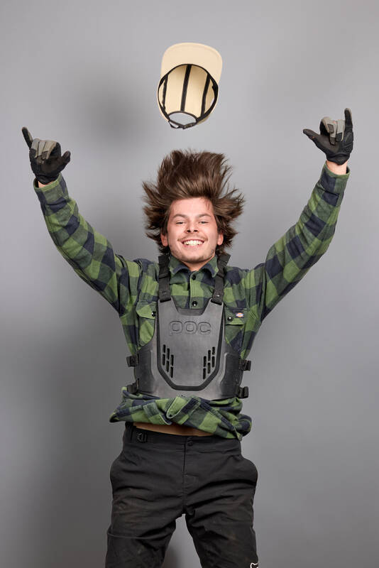 Foto eines jungen Mannes in Skater-Schutzausrüstung im Sprung vor grauem Studiohintergrund.