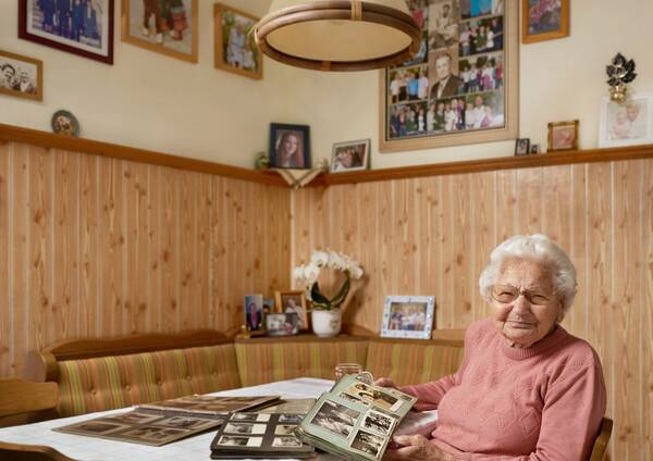 Eine alte Frau sitzt mit mehreren alten Fotoalben an einem Tisch.