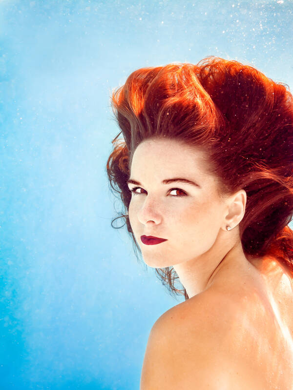 Portrait einer Frau mit wallenden roten Haaren unter Wasser. 