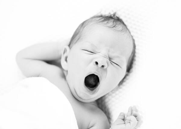 Ein Baby liegt im Bett und gähnt. Schwarz-Weiß.