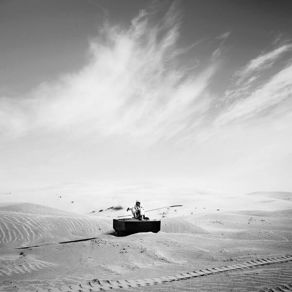 Ein Mann sitzt mitten in der Wüste auf den Resten eines alten Panzers. Schwarz-Weiß.