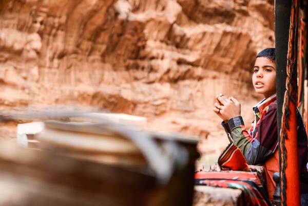 Ein Bub in buntem Hemd und mit gewebten Decken vor einer lehmigen Wand.