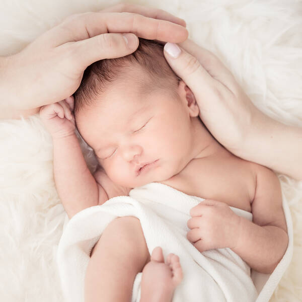 Ein Neugeborenes in einer Windel, die Mutter hat ihre Hände um den Kopf des Kindes gelegt