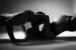 Silhouette eines Paares: Sie liegt auf dem Rücken und streckt den schwangeren Bauch in die Höhe. Ihre Hände legt sie dem Mann auf die Schultern, der sich im Stütz von hinten über ihren Kopf beugt und sie küsst. Beide sind nur mit Dessous bekleidet. Schwarz-Weiß.
