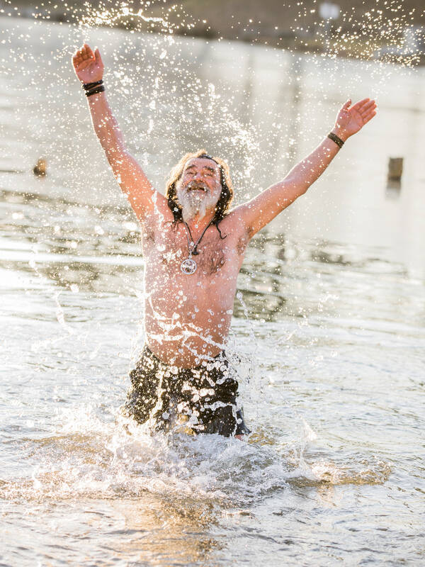 Ein älterer, bärtiger Mann tobt freudig im Wasser. 