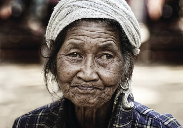 Portrait einer alten, ärmlich gekleideten Frau mit asiatischen Zügen und Kopftuch.