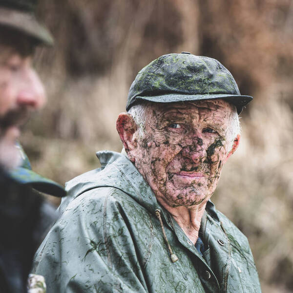 ein älterer Mann mit Kappe und Regenjacke ist völlig mit Algen bedeckt.