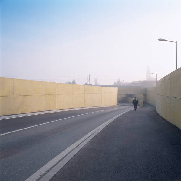 ein Mann in dunkler Kleidung und mit Hut geht durch die Bahnunterführung in Feldkirchen. Morgenstimmung mit letzten Nebelschleiern, die sich gerade lichten.