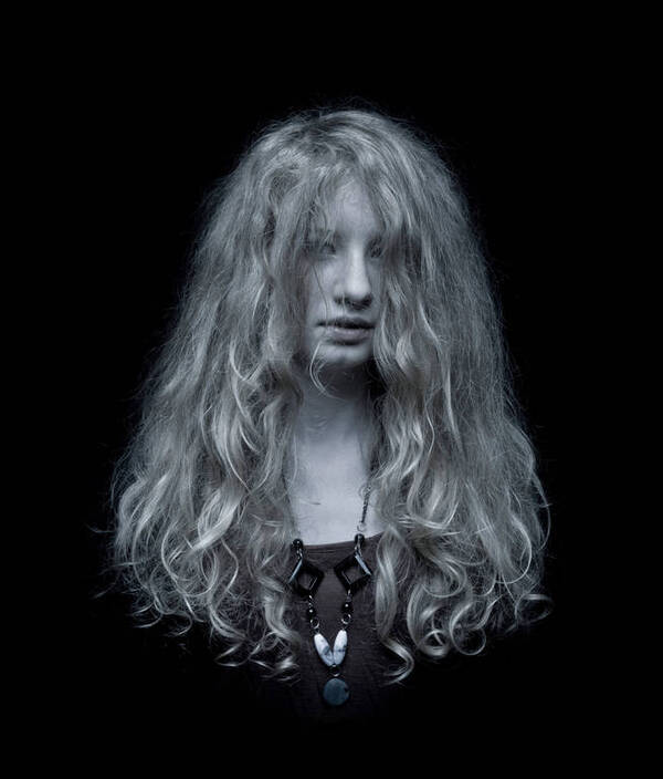 Blondes Mädchen mit langen lockigen Haaren vor schwarzem Hintergrund.