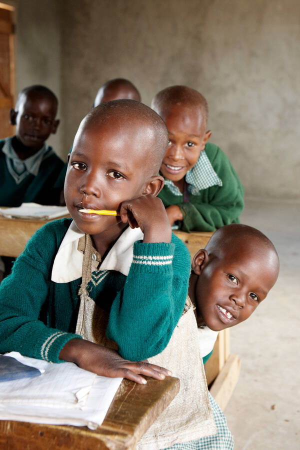 Dunkelhäutige, kahlgeschorene Kinder in Schuluniformen sitzen in alten Schulbänken.