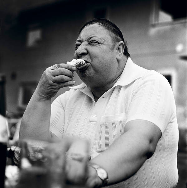 Ein beleibter Mann beißt in ein Brot. Schwarz-Weiß.