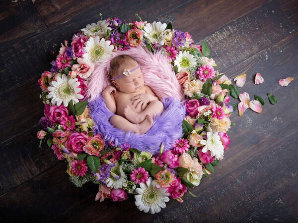 Ein neugeborenes Baby liegt schlafend in einem Blütenkranz.