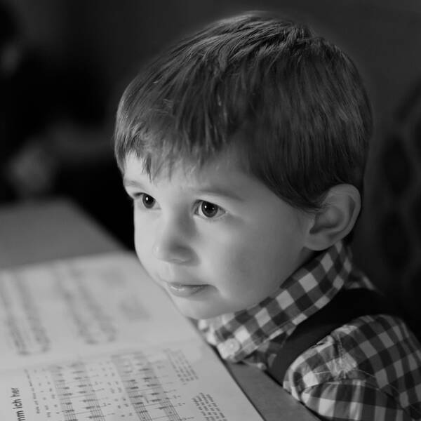 Ein kleiner Bub sitzt an einem Tisch und hat vor sich Weihnachtslieder-Noten ausgebreitet. Schwarz-Weiß.