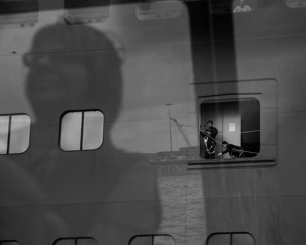 Reflexion einer Frau, die durch eine Scheibe Arbeiten gegenüber beobachtet. Schwarz-Weiß.